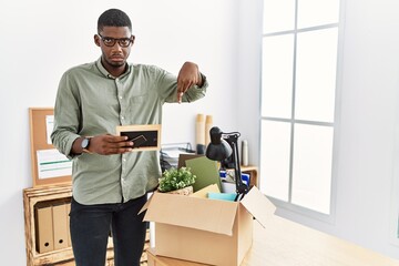 Sticker - Young african american businessman unboxing box at the office pointing down looking sad and upset, indicating direction with fingers, unhappy and depressed.