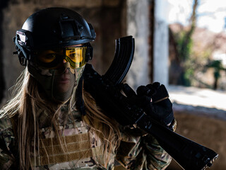 Portrait of a woman in a helmet and goggles with a machine gun in her hands. A female soldier in a camouflage uniform holds a weapon.