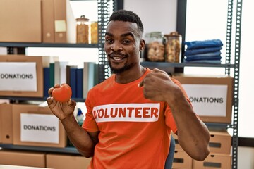 Sticker - Young african man wearing volunteer t shirt at donations stand holding heart pointing finger to one self smiling happy and proud