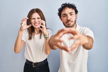 Poster - Young couple wearing casual clothes standing together shouting frustrated with rage, hands trying to strangle, yelling mad