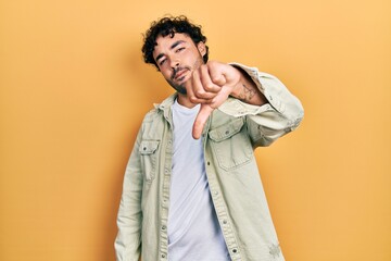 Wall Mural - Young hispanic man wearing casual clothes looking unhappy and angry showing rejection and negative with thumbs down gesture. bad expression.