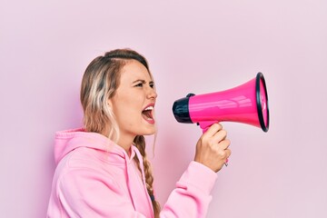 Wall Mural - Young beautiful blonde caucasian woman shouthing and screaming through megaphone over isolated pink background