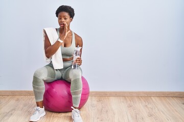 Sticker - African american woman wearing sportswear sitting on pilates ball hand on mouth telling secret rumor, whispering malicious talk conversation