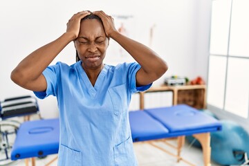 Wall Mural - Black woman with braids working at pain recovery clinic suffering from headache desperate and stressed because pain and migraine. hands on head.