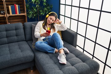 Wall Mural - Young hispanic woman listening to music sitting on sofa at home
