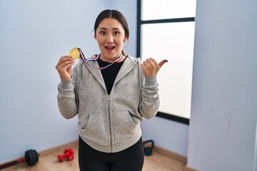 Sticker - Young latin woman wearing winner medal pointing thumb up to the side smiling happy with open mouth