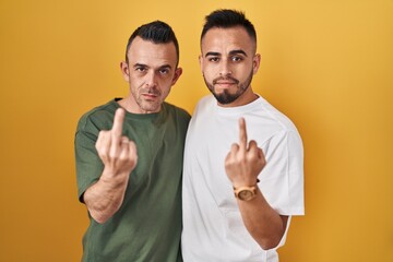 Canvas Print - Homosexual couple standing over yellow background showing middle finger, impolite and rude fuck off expression