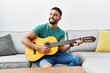 © Krakenimages.com - Young arab man playing classical guitar sitting on sofa at home