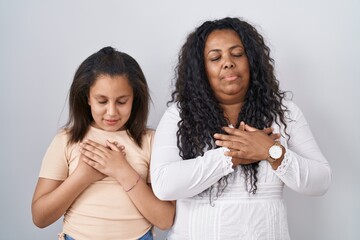 Poster - Mother and young daughter standing over white background smiling with hands on chest with closed eyes and grateful gesture on face. health concept.