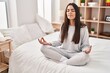 © Krakenimages.com - Young hispanic woman doing yoga exercise sitting on bed at bedroom