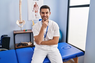 Sticker - Young hispanic man with beard working at pain recovery clinic looking confident at the camera with smile with crossed arms and hand raised on chin. thinking positive.