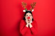 Leinwandbild Motiv Young hispanic woman wearing deer christmas hat and red nose afraid and shocked, surprise and amazed expression with hands on face