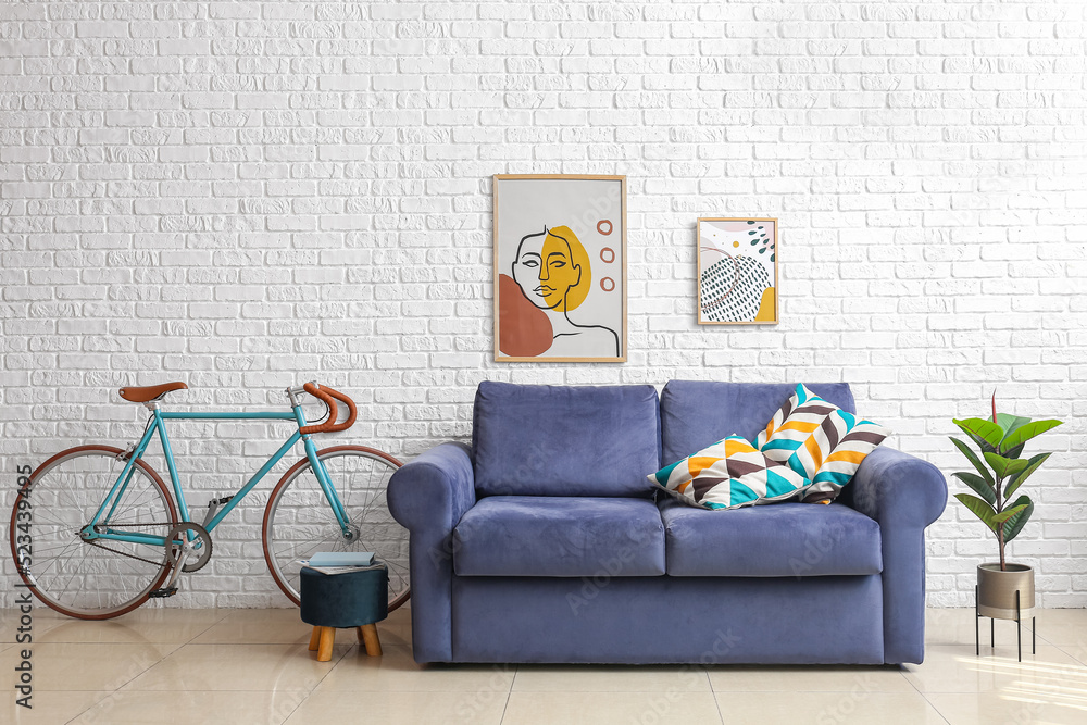 Bicycle, blue sofa, pouf and houseplant near white brick wall