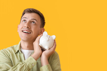 Canvas Print - Young man with white piggy bank on yellow background