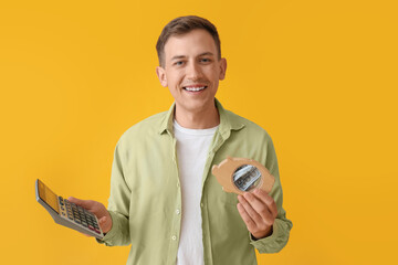 Canvas Print - Young man with piggy bank and calculator on yellow background