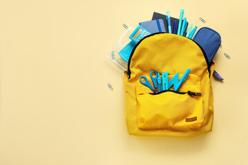 Yellow backpack with school stationery on beige background