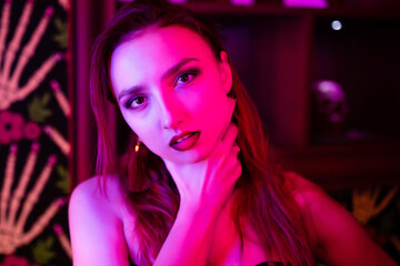 Portrait of a beautiful girl in a corset. Purple lighting. She looks seductively into the camera with her hand on her neck. Halloween concept, nightclub, masquerade