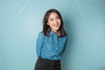 Wall Mural - A portrait of a happy Asian woman is smiling and wearing a blue shirt isolated by a blue background