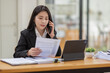 © David - Business Asian woman talking on the phone and working with laptop calculator document on an office desk, planning analyzing the financial report, business plan investment, finance analysis concept.