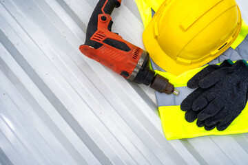 An orange drill, a yellow plastic cap and mechanic gloves resting on a white metal sheet roof.