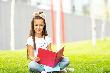 Wall Mural - Cute Little Girl Reading Book Outside on Grass