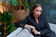 Young attractive business woman sitting in a cafe on a sofa in a black suit looks thoughtfully into the camera brunette