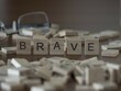 Brave word or concept represented by wooden letter tiles on a wooden table with glasses and a book