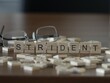 Strident word or concept represented by wooden letter tiles on a wooden table with glasses and a book