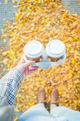 Woman hands holding two cups of takeaway coffee on autumn yellow leaves background with copy space