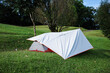 White flysheet cover tent on green grass ground in forest.