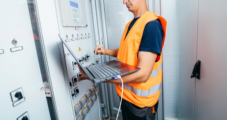 Wall Mural - Adult electrician builder engineer testing and screwing equipment in fuse box and repairing of modern electricity power station. Automatic control cabinet