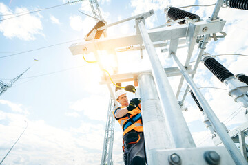 Electrician in protective helmet working on high voltage power lines. Highly skilled workmen servicing the electricity grid. Modern power station with power towers