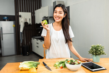 Wall Mural - Young female eating greens apple in weight loss diet and wellness on table. Beautiful woman happily eat a healthy salad breakfast in kitchen in the morning. Diet food concept.