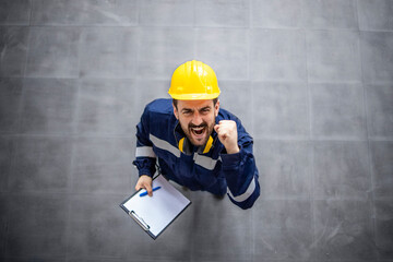 Wall Mural - Top view of happy factory worker in protective work wear and hardhat celebrating job results, promotion and success.