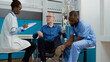 © DC Studio - Doctor and nurse consulting patient with chronic impairment, doing physiotherapy and alternative medicine to help with physical disability. Medical staff at checkup with wheelchair user.