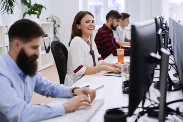 Junior female professional working in modern IT office. Group of young and experienced programmers and software developers sitting at desks working on computers.