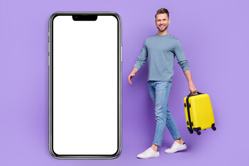 Poster - Photo of excited cute guy wear grey shirt holding suitcase walking modern device empty space isolated violet color background