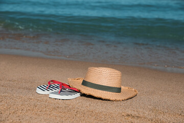 Canvas Print - Stylish straw hat and striped flip flops on sandy beach near sea