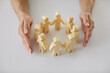 © Studio Romantic - Human hands protecting and guarding small wooden toy figures placed on white desk as metaphor for creating safe, supportive community of people. Close up, closeup shot. Care, support, safety concepts