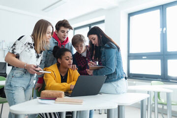 Wall Mural - high school students sitting together at desk and using laptop and talking during break in classroom