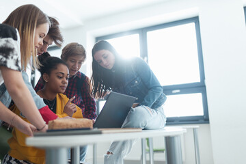 Wall Mural - high school students sitting together at desk and using laptop and talking during break in classroom