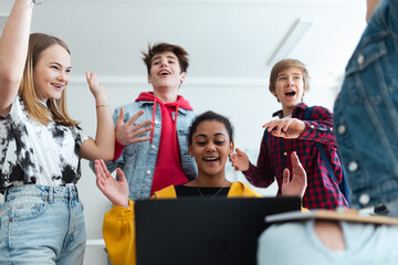 Wall Mural - High school students sitting together at desk and using laptop and talking during break in classroom.