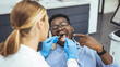 © Dragana Gordic - Young black man holding cheek in chair at dentist, having toothache. Young good looking man having dental treatment at dentist's office. Unhappy african american man in medical chair complains