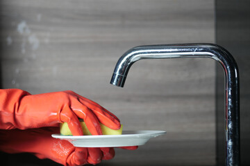 Sticker - sponge , hand in red rubber gloves cleaning a plate with sponge 