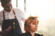 © chokniti - Smiling young woman curling hair with machine by male stylist in modern salon for a hairdo and new fashion trend
