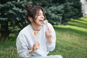 Wall Mural - A young woman eating sushi in the park, picnic in nature.