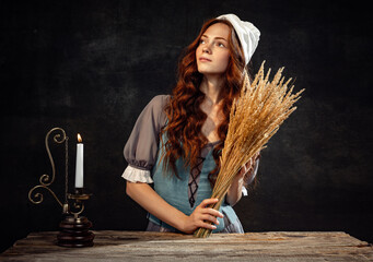 Creative portrait of young beautiful redhead girl with long curly hair in image of medieval person in renaissance style dress isolated on dark background.