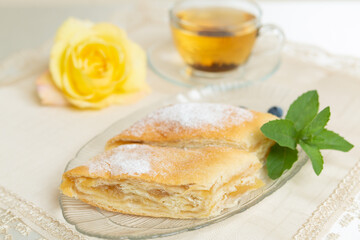 There are two slices of apple pie, blueberries and mint leaves on the plate, a cup of tea next to it, and the table is decorated with a live rose