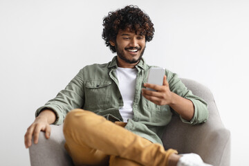 Wall Mural - Cheerful hindu guy using cell phone over white