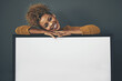 © Camerene Pendl/peopleimages.com - Woman standing with blank sign or portrait frame, showing copy space for advertising or marketing on dark background. Happy, smiling and relaxed Afro female portrait with big white poster copyspace